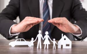 A real estate attorney holding his hands of a family, car, and house cut out of paper