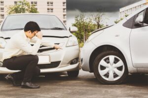 A businessman in a suit points toward a company car involved in a wreck in front of him.